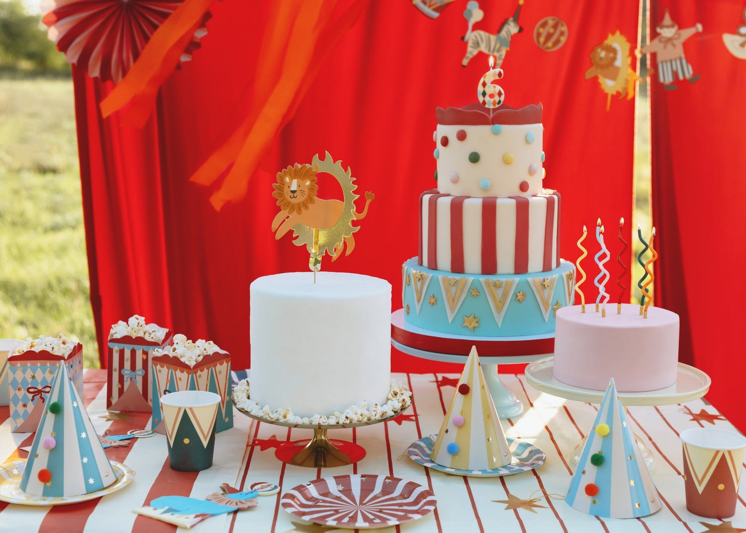 Children dressed in circus-themed costumes posing outdoors at a birthday party, surrounded by colorful circus decorations, balloons, and a red birthday table backdrop with 'Happy Birthday' banner