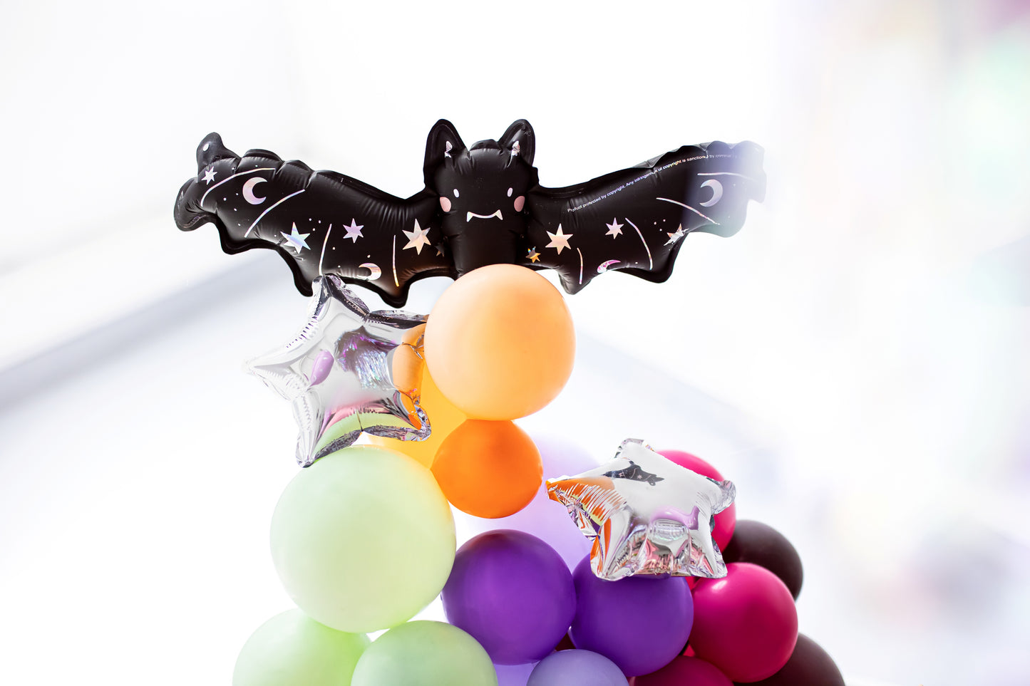 Decorative wand with bat design and colorful balloons on a white background