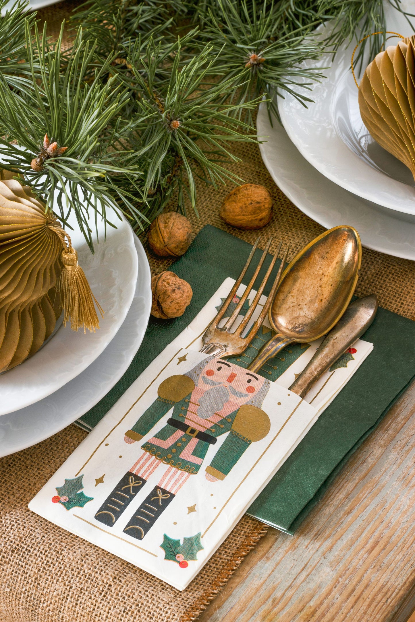 Christmas-themed place setting with nutcracker design on a card, gold cutlery, and green napkin.