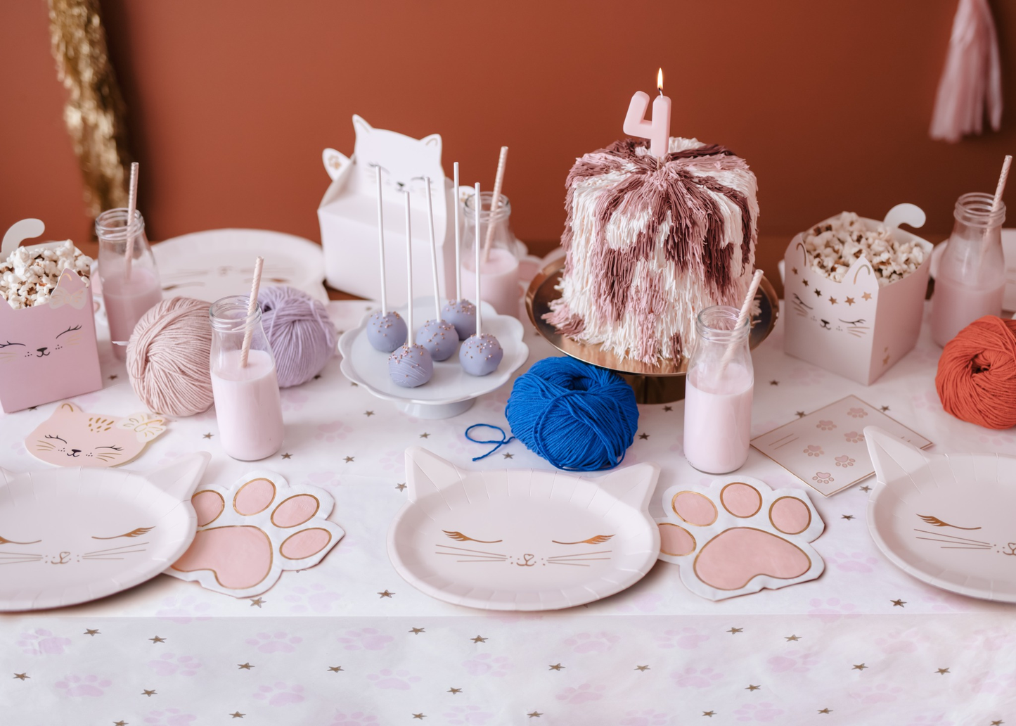 Adorable cat-themed birthday table setup with kitty plates, paw napkins, pastel snack boxes, pink milk, yarn decor and a fluffy pink cake with number 4 candle, perfect for a kids cat party.