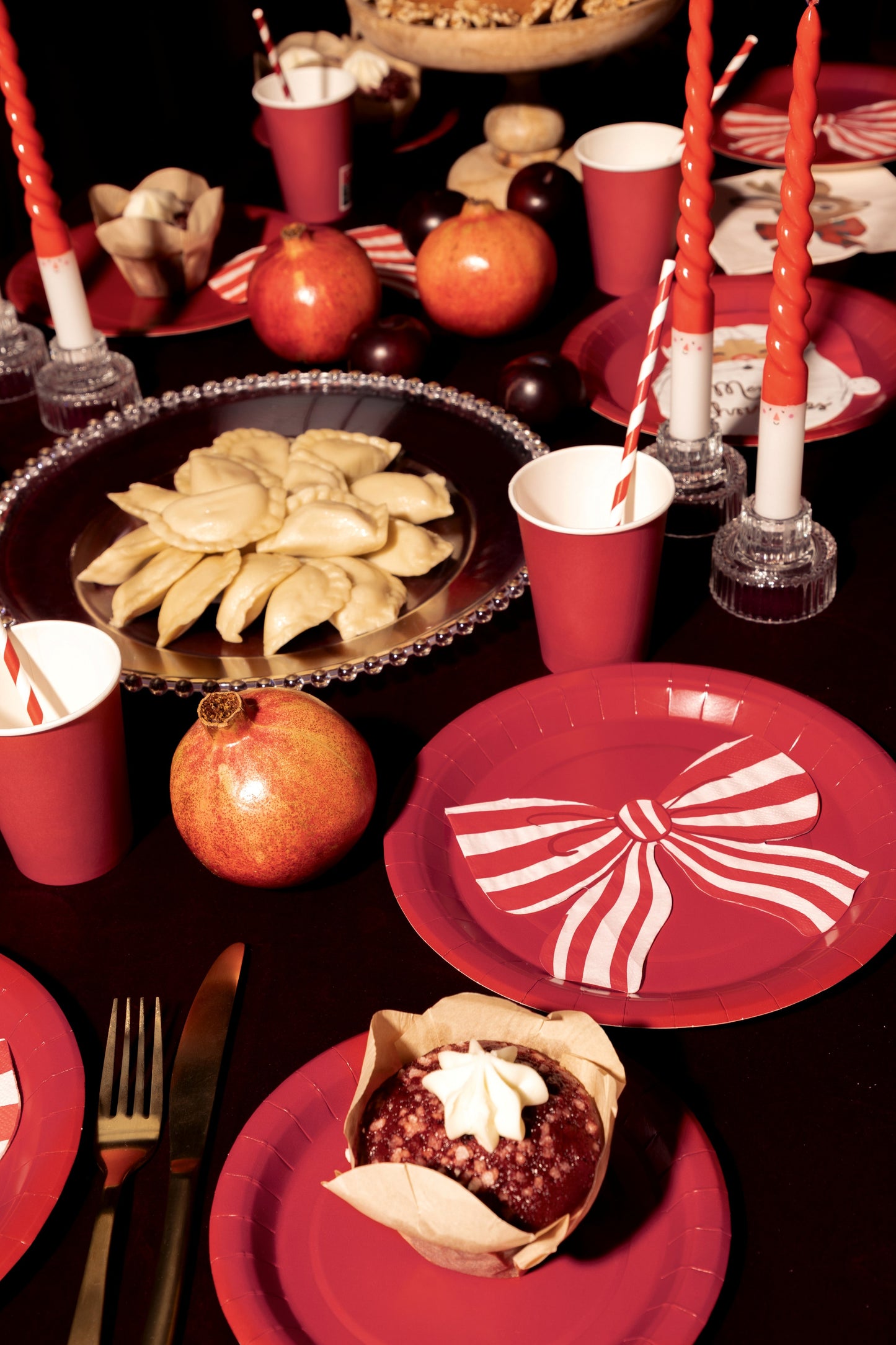 Dessert table setting with red plates, bowls, and cups, featuring a dessert and pomegranates.