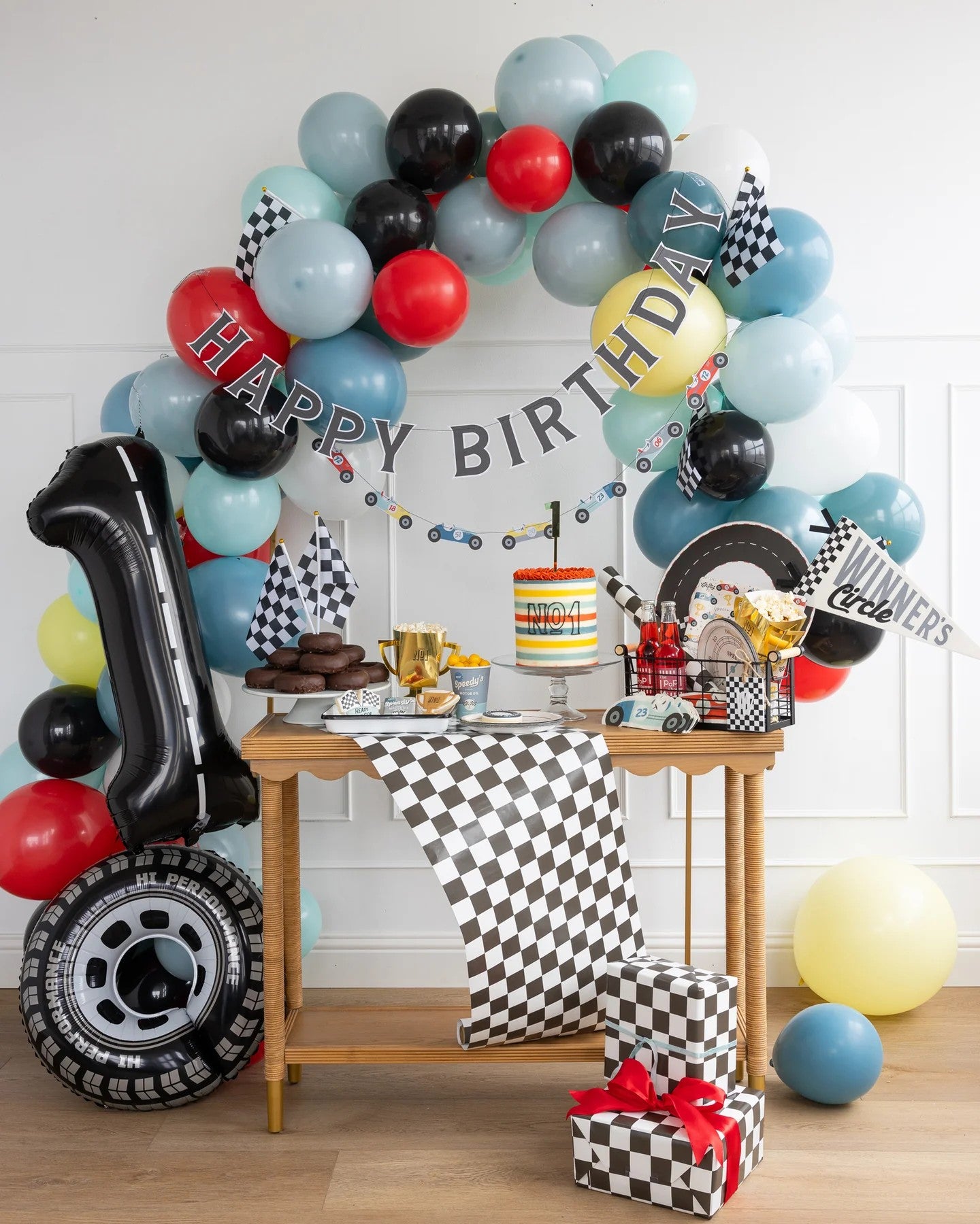 Birthday party racing cars setup with balloons, cake, and decorations in a room.
