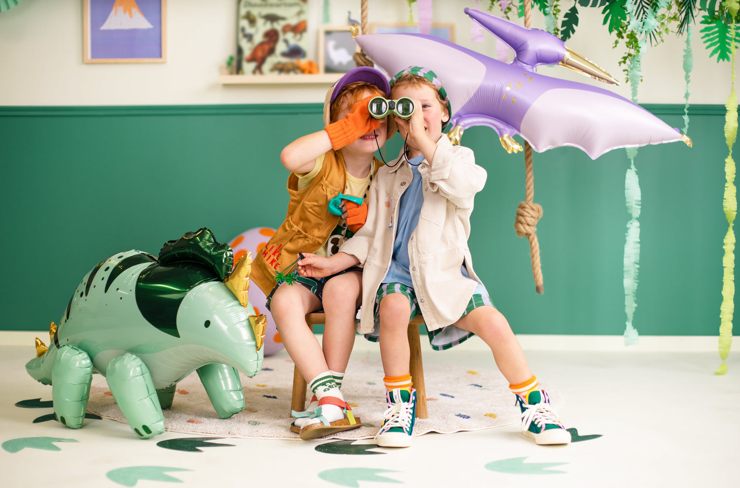 Dino Fun birthday party decorations, dinosaur balloons, Happy Birthday garland, plates, and table decorations in a green and pastel setting