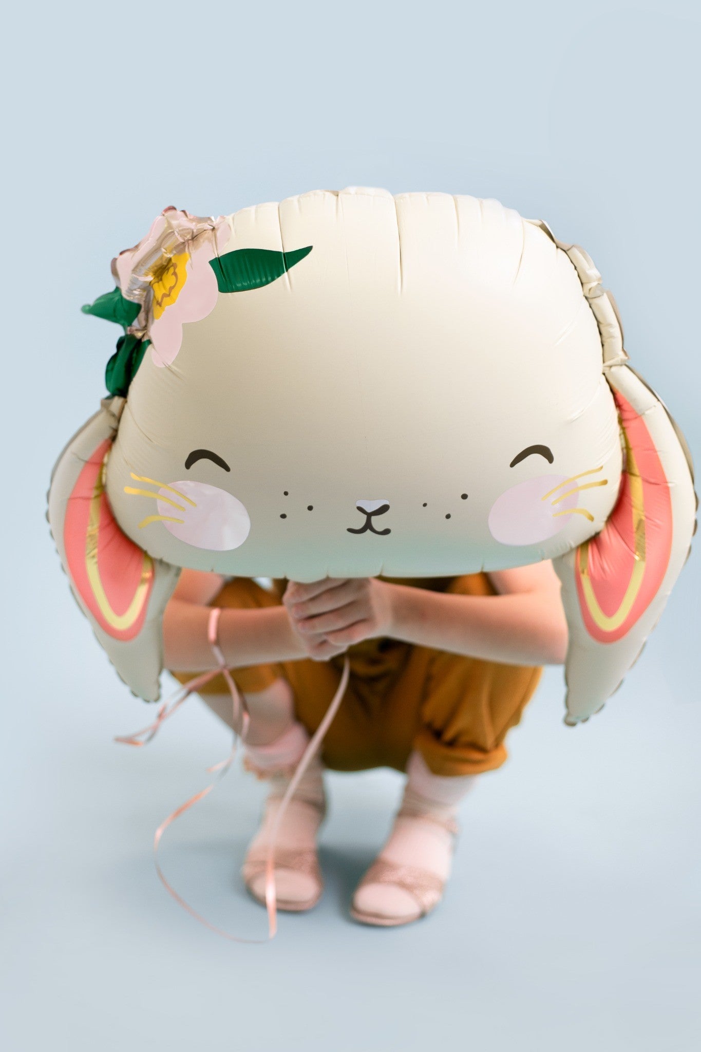 Girl holding a large bunny foil balloon in front of her face, pastel background