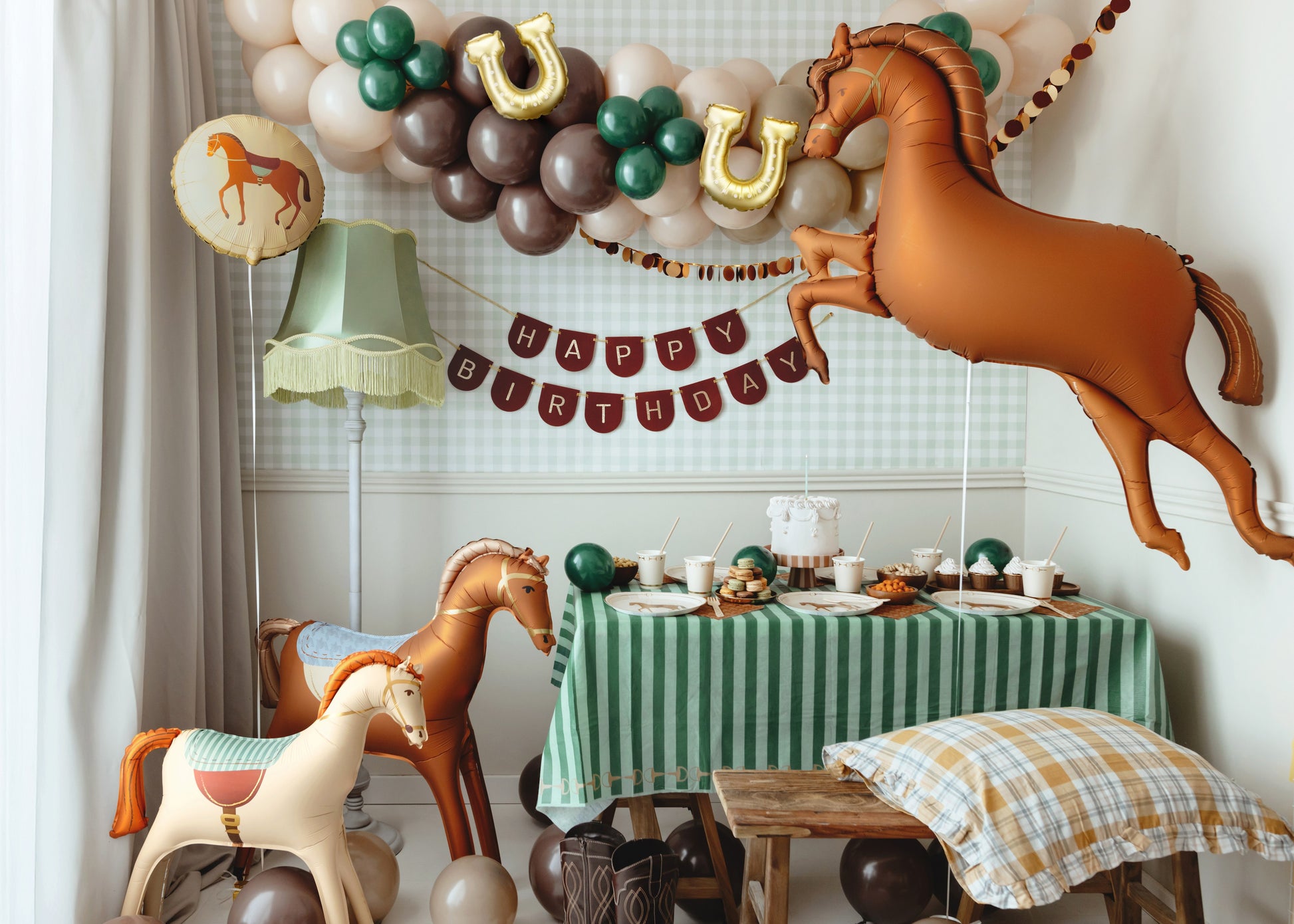Horse-themed birthday party setup with inflatable horse balloons, 'Happy Birthday' banner, brown and green balloon garland, and rustic table decor