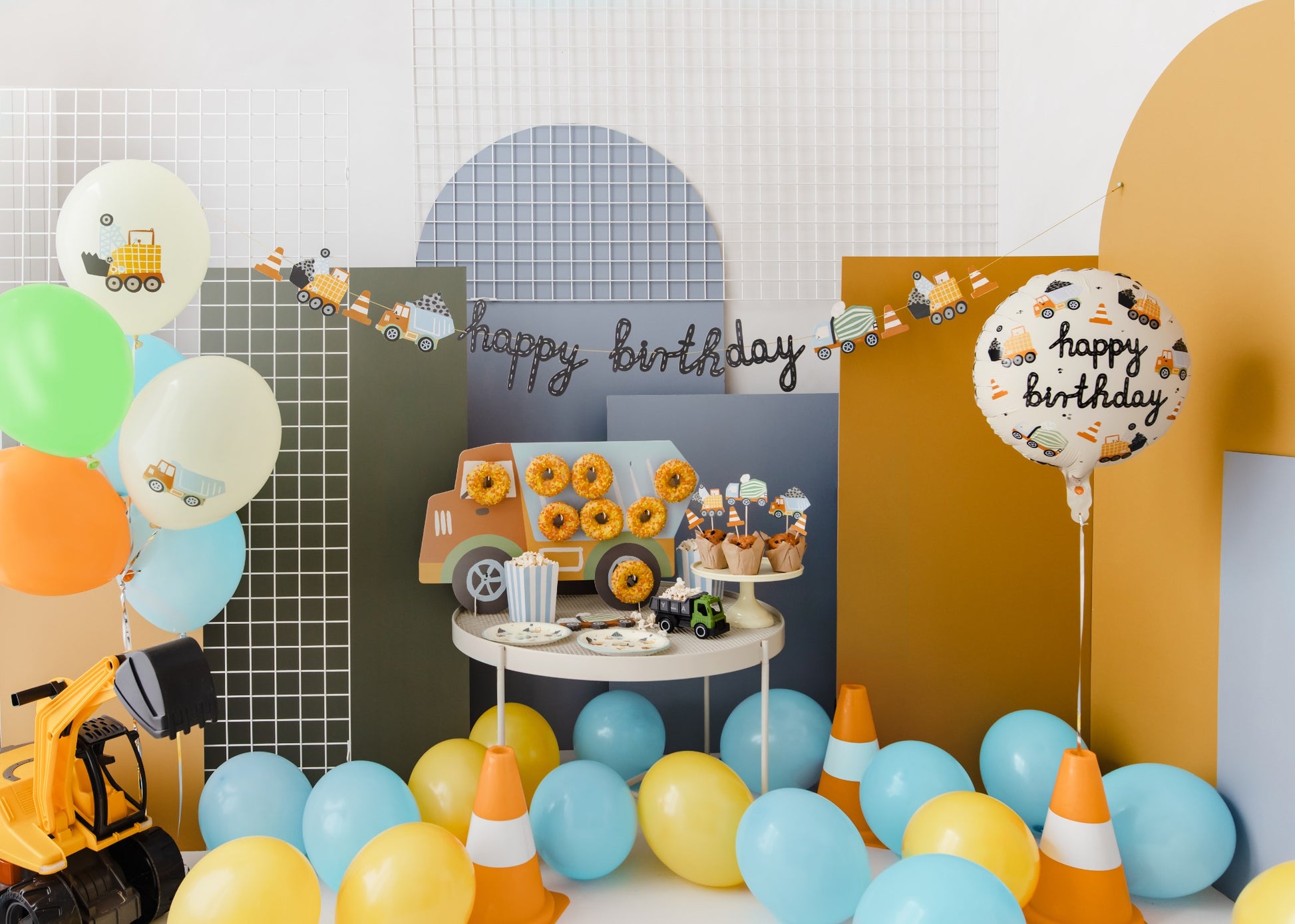Colorful latex balloons decorated with construction vehicle illustrations, displayed with orange traffic cones and toy trucks