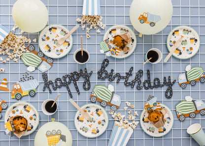 Party table decorated with construction-themed paper plates, cups, popcorn, and 'Happy Birthday' banner, ideal for birthday celebrations