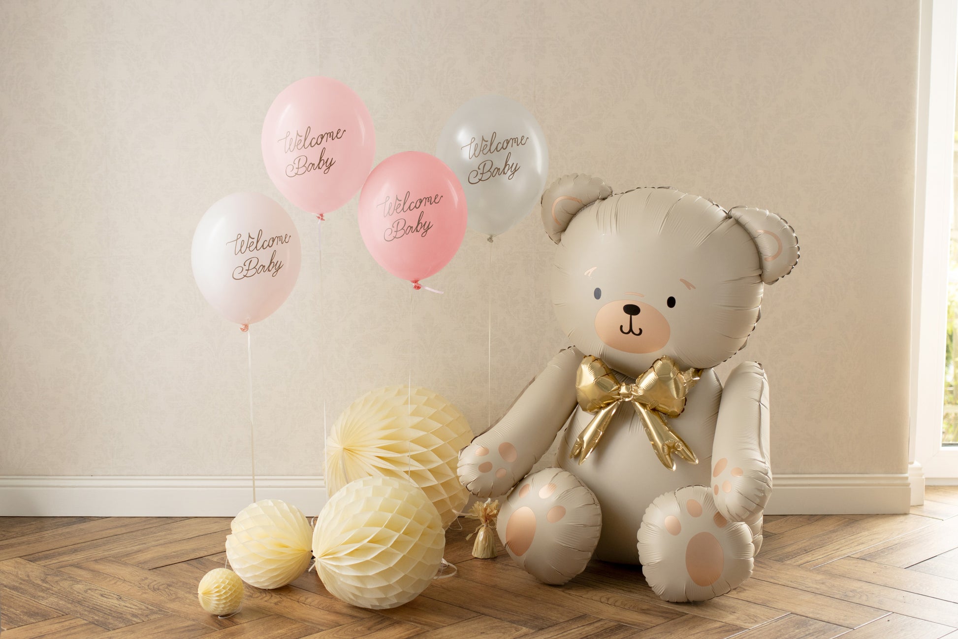 Teddy bear balloon with 'Welcome Baby' balloons and decorations on a wooden floor.