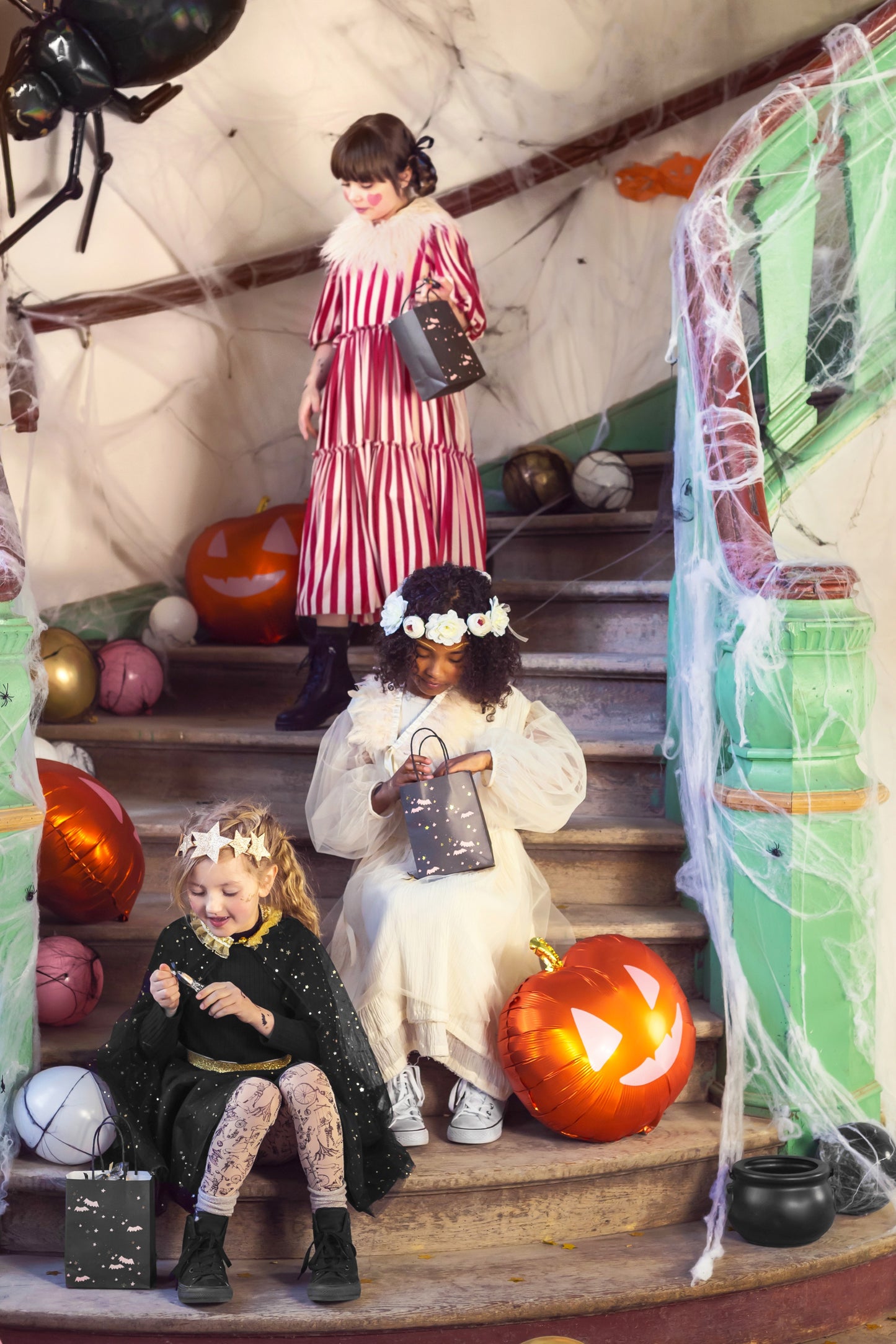 Children in Halloween costumes on a staircase with pumpkins and spider decorations.