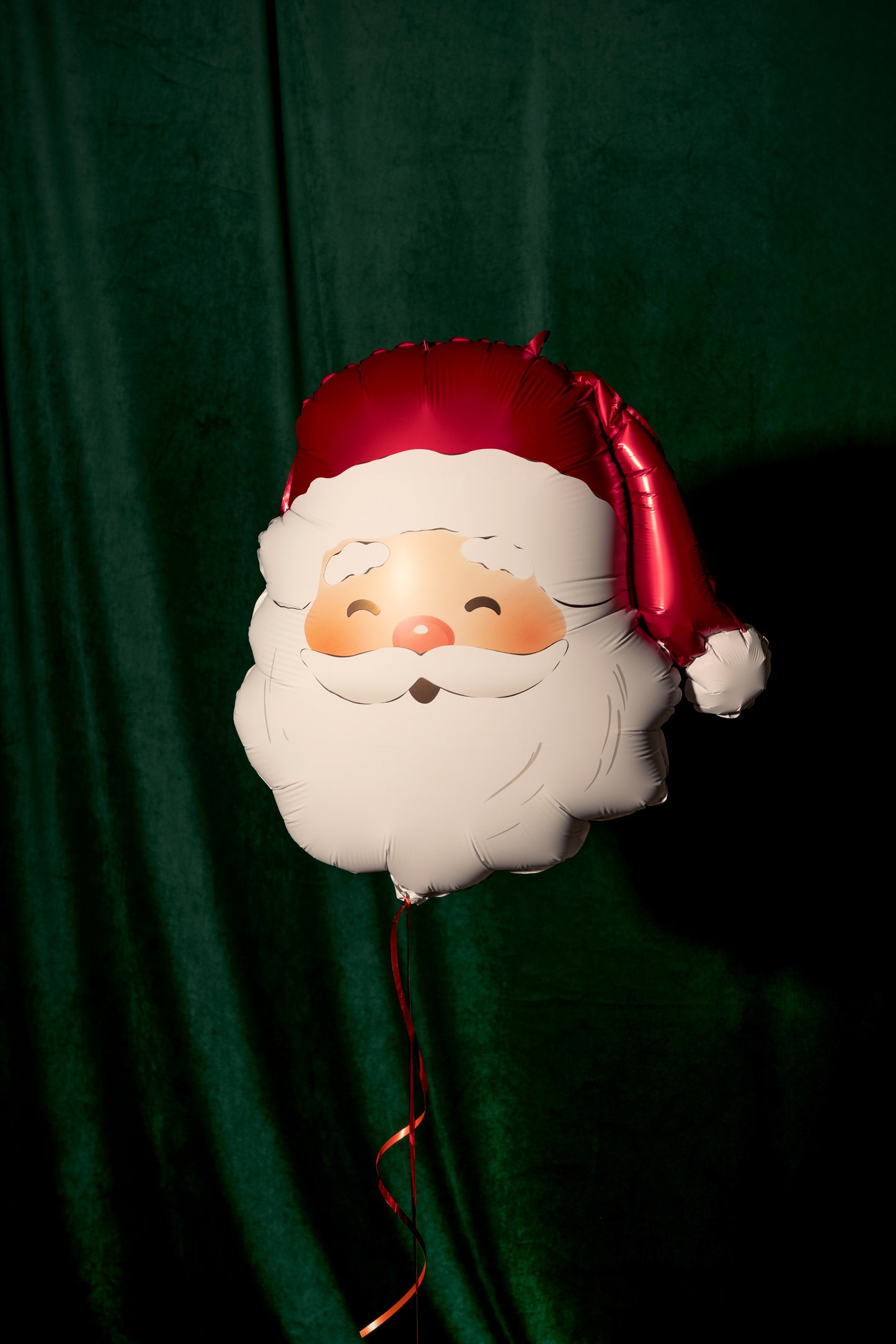 Balloon shaped like a Santa Claus face against a green curtain background