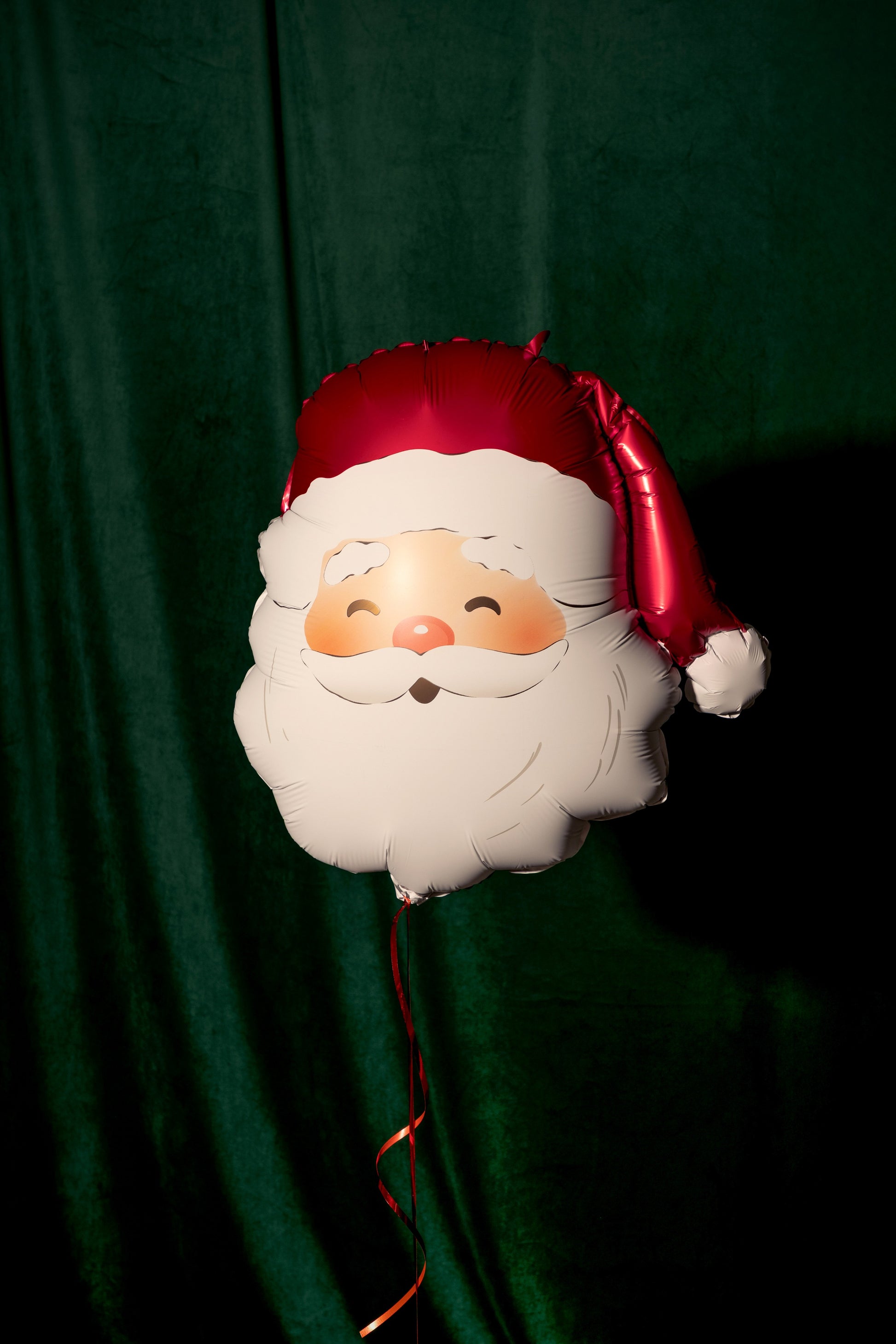 Balloon shaped like a Santa Claus face against a green curtain background