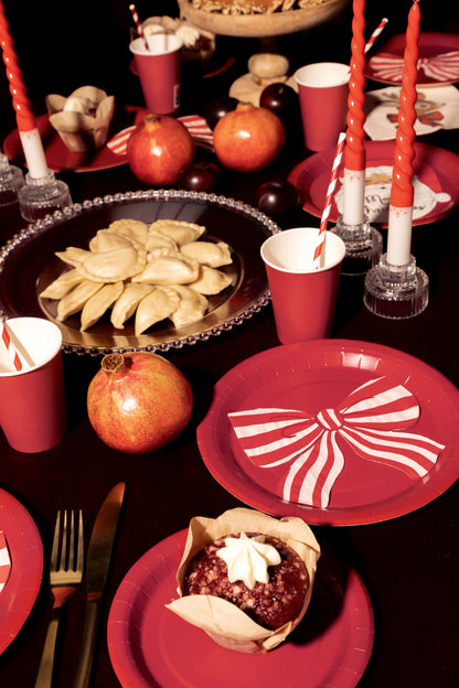 Dessert table setting with red plates, bowls, and cups, featuring a dessert and pomegranates.