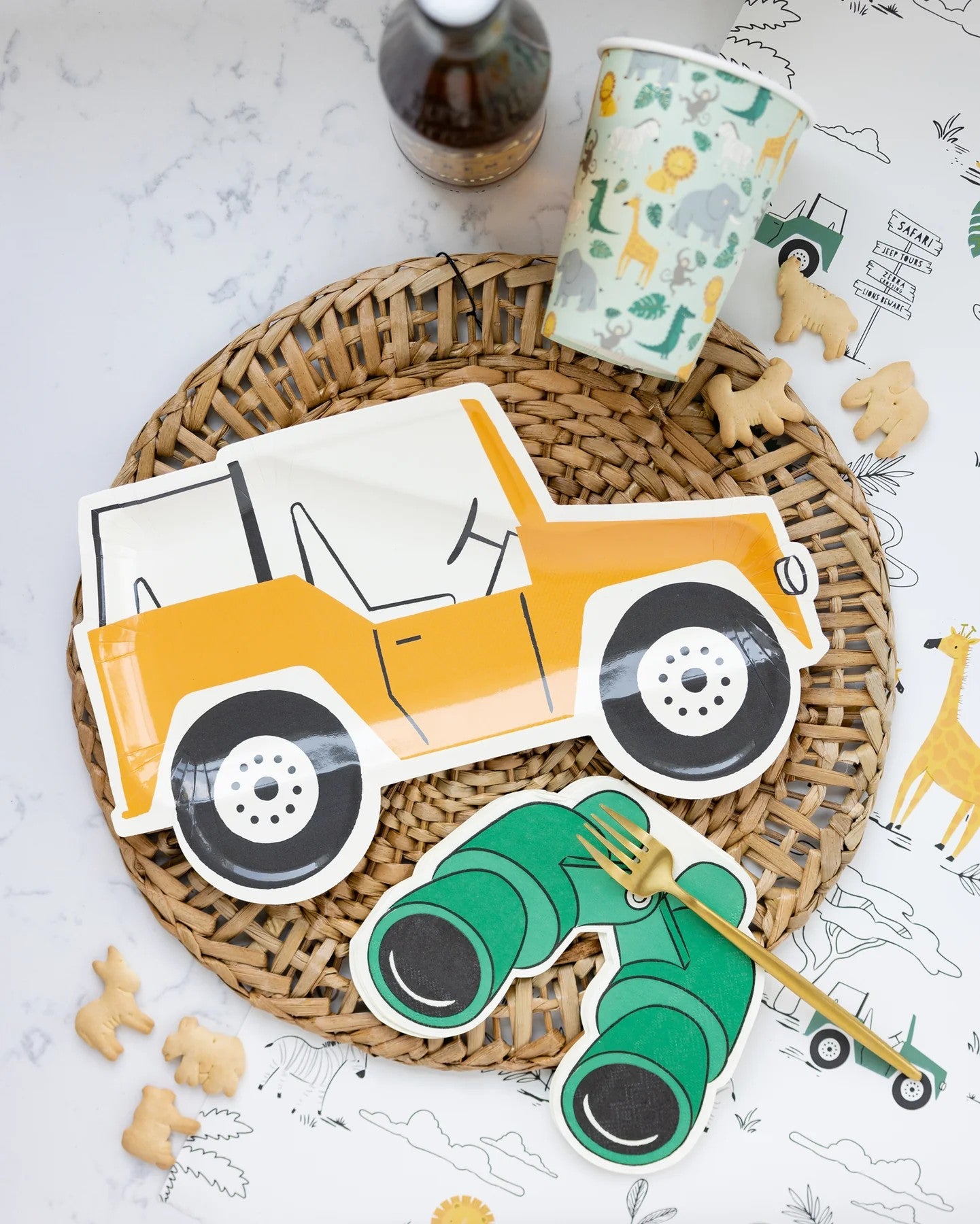 Paper plates of a yellow car and green binoculars on a woven mat with a marble surface.